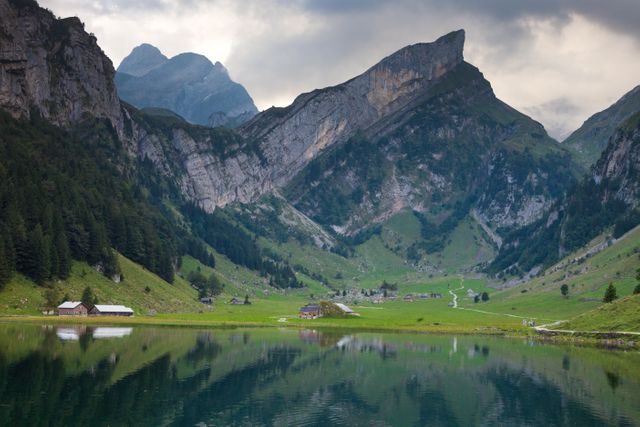Quiet Alpine valley with a lake reflecting surrounding mountains and green landscape. Ideal for travel websites, nature photography, hiking, outdoor activities, tranquility, vacation destinations in Swiss Alps.