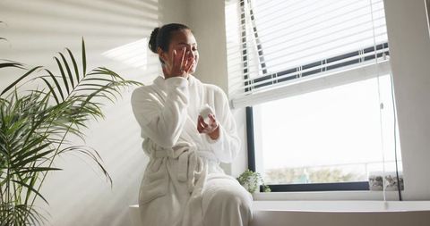 Serene asian woman applying moisturizer on bathtub ledge skincare ritual in natural light