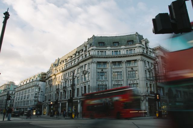 Street view showcasing iconic London double-decker buses against a backdrop of classic architectural buildings in an urban setting. Ideal for use in travel articles, cultural content, or marketing materials promoting tourism in London.