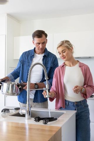 Couple filling pot at modern kitchen sink with chrome spring faucet