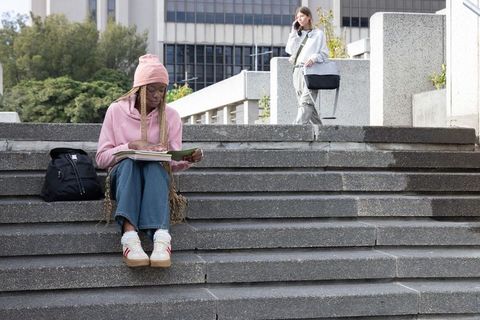 College students studying on concrete steps reading notes while friend making phone call