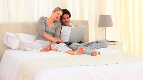 Couple Relaxing with Laptop in Bright Bedroom