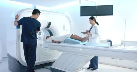 Technician adjusting mri scanner while clinician reviewing tablet with patient on table