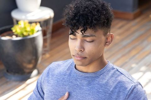 Young man meditating on sunlit terrace with hand on chest, serene mindfulness portrait