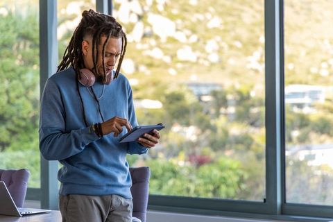 African american man using tablet and wearing headphones in bright modern home office