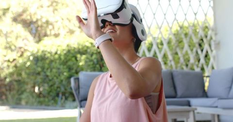 Woman wearing vr headset reaching outdoors on patio showing smart wrist wearable at home