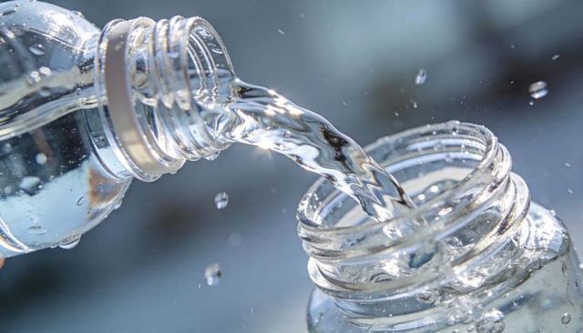 Pouring clear water between plastic bottle necks close-up sunlit sparkling droplets