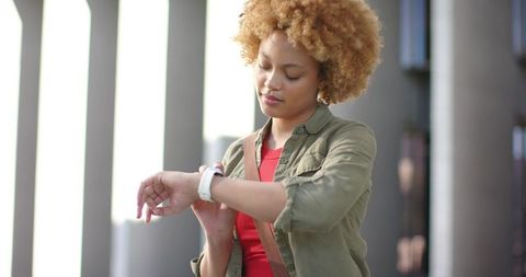African American woman checking smartwatch at modern urban plaza with architectural columns