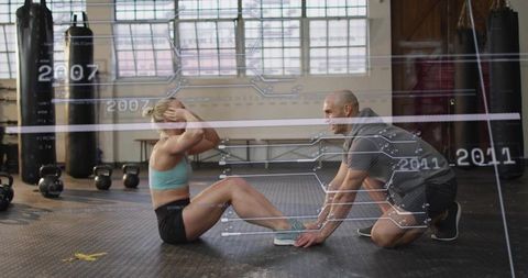 Trainer holding feet as athlete performing sit-ups with AR fitness overlay in industrial gym