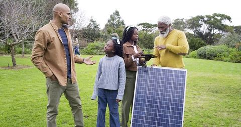 Multigenerational Black family examining solar panel and consulting tablet in garden