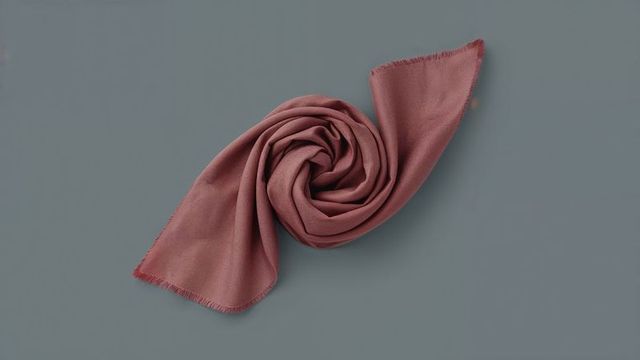 Elegant spiral folded burgundy scarf on gray-blue background