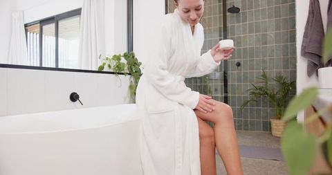 Woman in Bathrobe Using Lotion in Modern Minimalist Bathroom