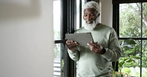 Senior Man Enjoying Technology on Tablet by Window at Home