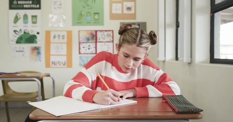 Focused girl student writing in notebook at school desk