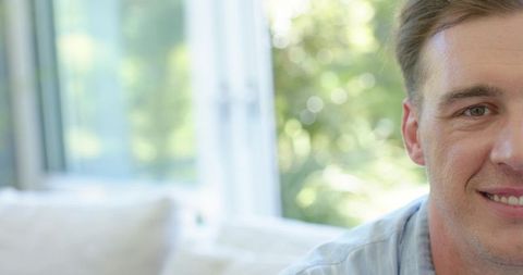 Smiling man relaxing at home by sunny window with blurred garden bokeh and cozy sofa