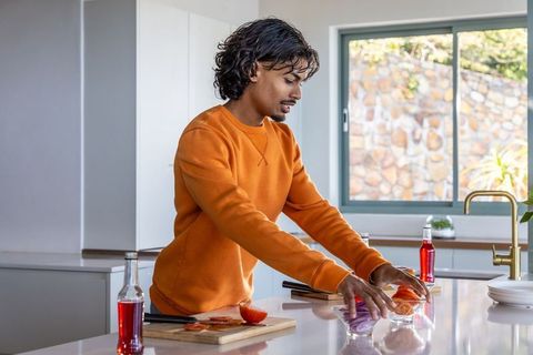 Young man preparing tomatoes on modern kitchen island wearing orange sweatshirt