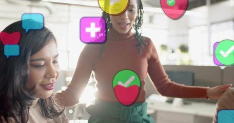 Women collaborating at desk in modern office with floating social icons showing feedback