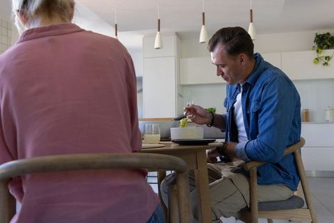 Couple sharing meal at kitchen table, man eating pasta in minimalist open-plan kitchen