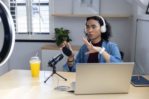 Non-binary creator livestreaming and recording podcast with headphones, mic, laptop, ring light