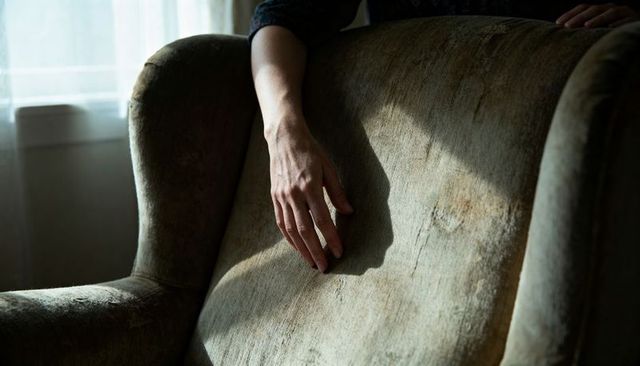 Resting hand draping over worn armchair in sidelight, intimate contemplative interior