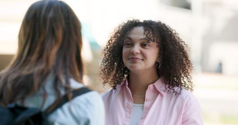 Curly student smiling and chatting with friend on sunny campus plaza casual conversation