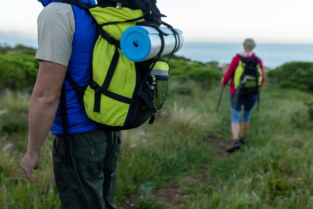 Senior couple hiking on a mountain trail with backpacks and hiking poles. Ideal for promoting outdoor activities, healthy lifestyles, and adventure travel for seniors. Can be used in advertisements for hiking gear, travel agencies, and fitness programs targeting older adults.