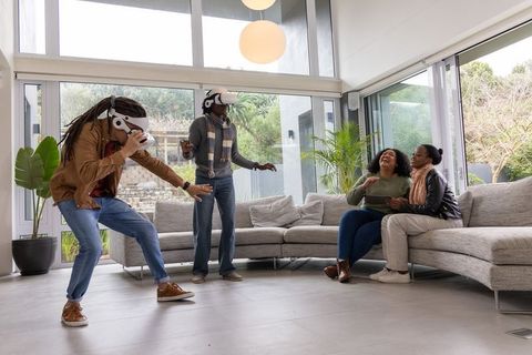African american friends playing virtual reality games in modern living room, laughing