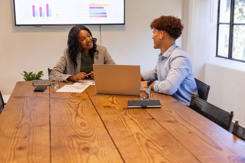 Diverse coworkers collaborating over charts and analytics at wooden table with laptop