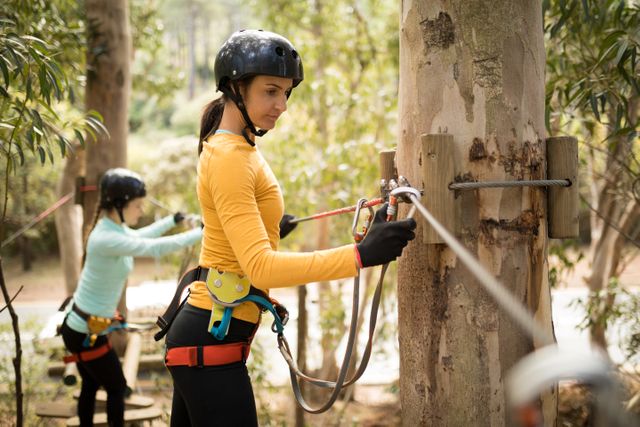 Woman participating in a zipline activity in an adventure park, wearing safety gear including a helmet and harness. Ideal for promoting outdoor activities, adventure parks, team-building events, and recreational sports. Perfect for use in travel brochures, adventure tourism websites, and fitness blogs.