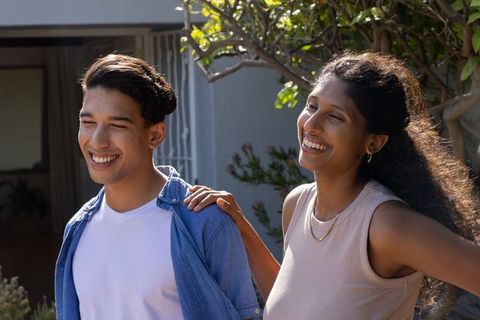 African american couple laughing on sunny porch near home security gate with greenery