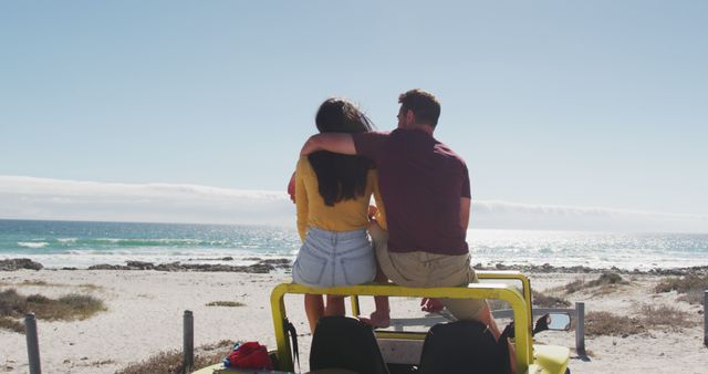 Couple enjoying a scenic ocean view sitting on top of a yellow jeep at a beach, embracing each other and looking at the horizon. Ideal for concepts related to romance, travel, summer vacations, relaxation, and adventure branding.