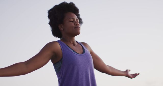 Woman is outdoors with eyes closed and arms stretched in a meditative and relaxed pose. This can be used for promoting mental health, serenity, mindfulness practices, breathing exercises, wellness retreats, self-care routines, fitness, and healthy lifestyles.