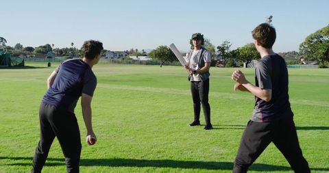 Young men playing casual cricket on sunny park grass field, batsman wearing laurel wreath