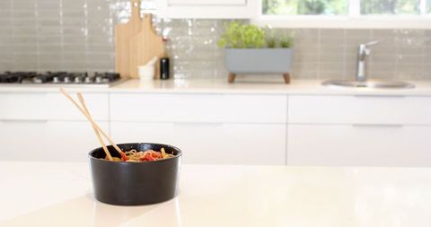 Black bowl of pasta on white counter in modern kitchen