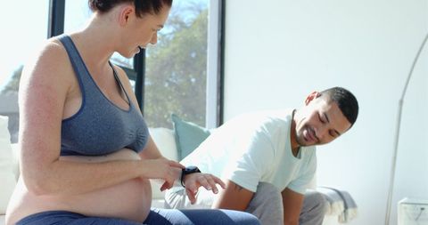 Expectant Couple Relaxing Together Checking Smartwatch at Home