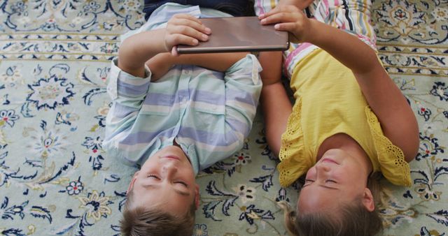 Happy caucasian brother and sister at home, lying on floor using tablet together and smiling. happy family, free time at home.