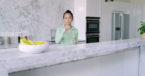 Woman in Minimalist Kitchen Holding Glass at Marble Island