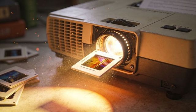 Retro slide projector casting warm light and dust motes over tabletop with 35mm slides