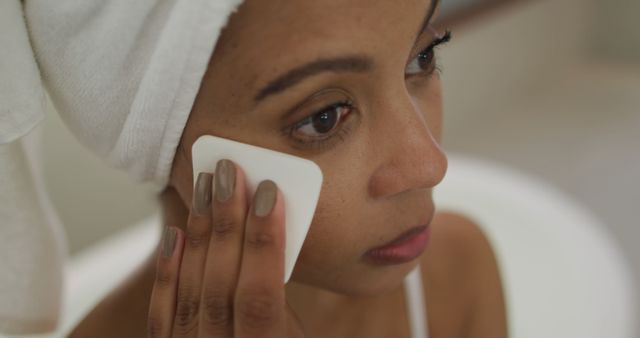 Biracial woman wearing towel on head cleaning her face. domestic life, spending quality free time relaxing at home.