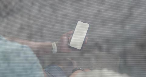 Man checking smartphone through semi-transparent mesh while sitting on urban bench, top-down
