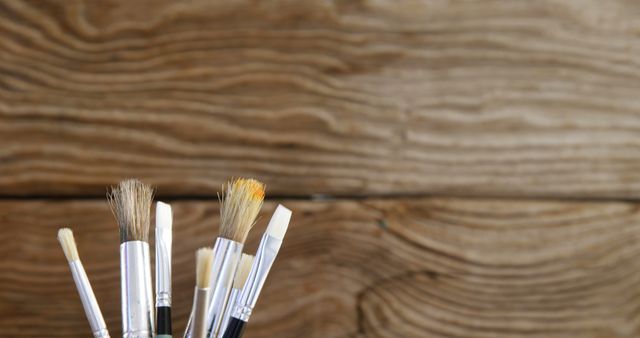 Various paintbrushes are in a holder against an empty wooden backdrop. Useful for representing artistic tools, art lessons, painting workshops, creativity, and DIY projects. Ideal for blogs, workshops, featured imagery, or promotional materials for art supply stores.