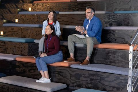 Colleagues attending seminar on tiered seating in modern collaborative office amphitheater
