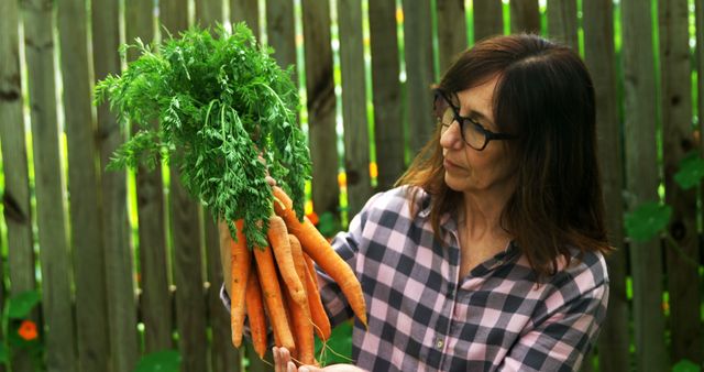 Caucasian woman holding carrots in garden with copy space. Hobby, gardening, lifestyle, relaxing, free time and domestic life concept, unaltered.