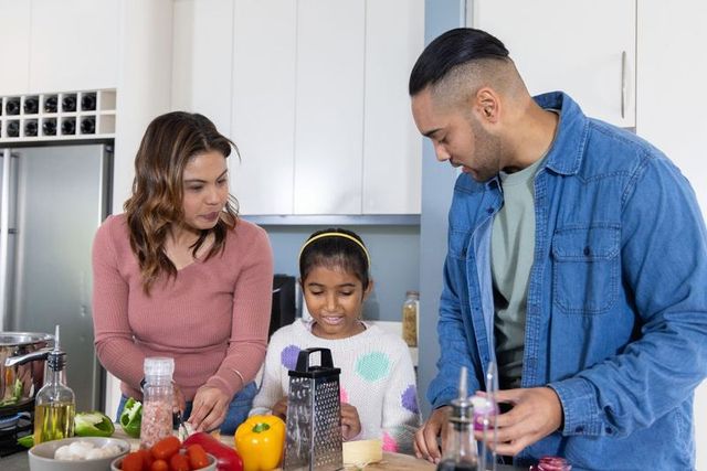 Diverse family cooking at kitchen island, chopping vegetables and grating cheese together