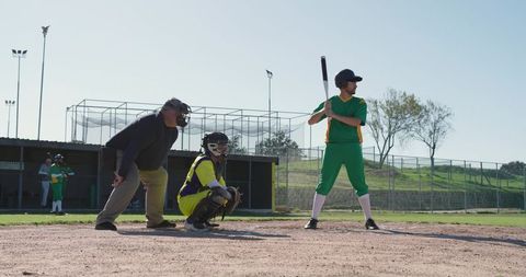 Batter at plate with catcher and umpire awaiting pitch on sunny baseball diamond