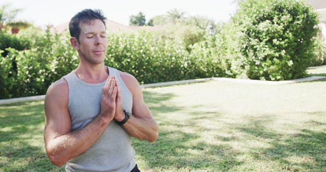 Man practicing yoga in outdoor garden, displaying peaceful and concentrated demeanor. Suitable for wellness, fitness, meditation, and outdoor lifestyle themes.