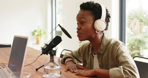 Black woman recording podcast at home studio with headphones and desktop microphone