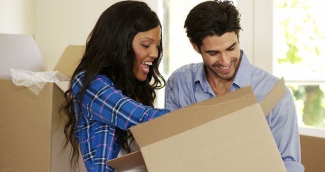 Young couple assisting each other while unpacking carton boxes in new house 4k