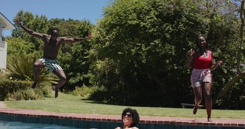 African American friends jumping, running and lounging by backyard pool on sunny summer day