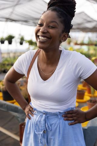Laughing african american woman at greenhouse nursery hands on hips casual summer style